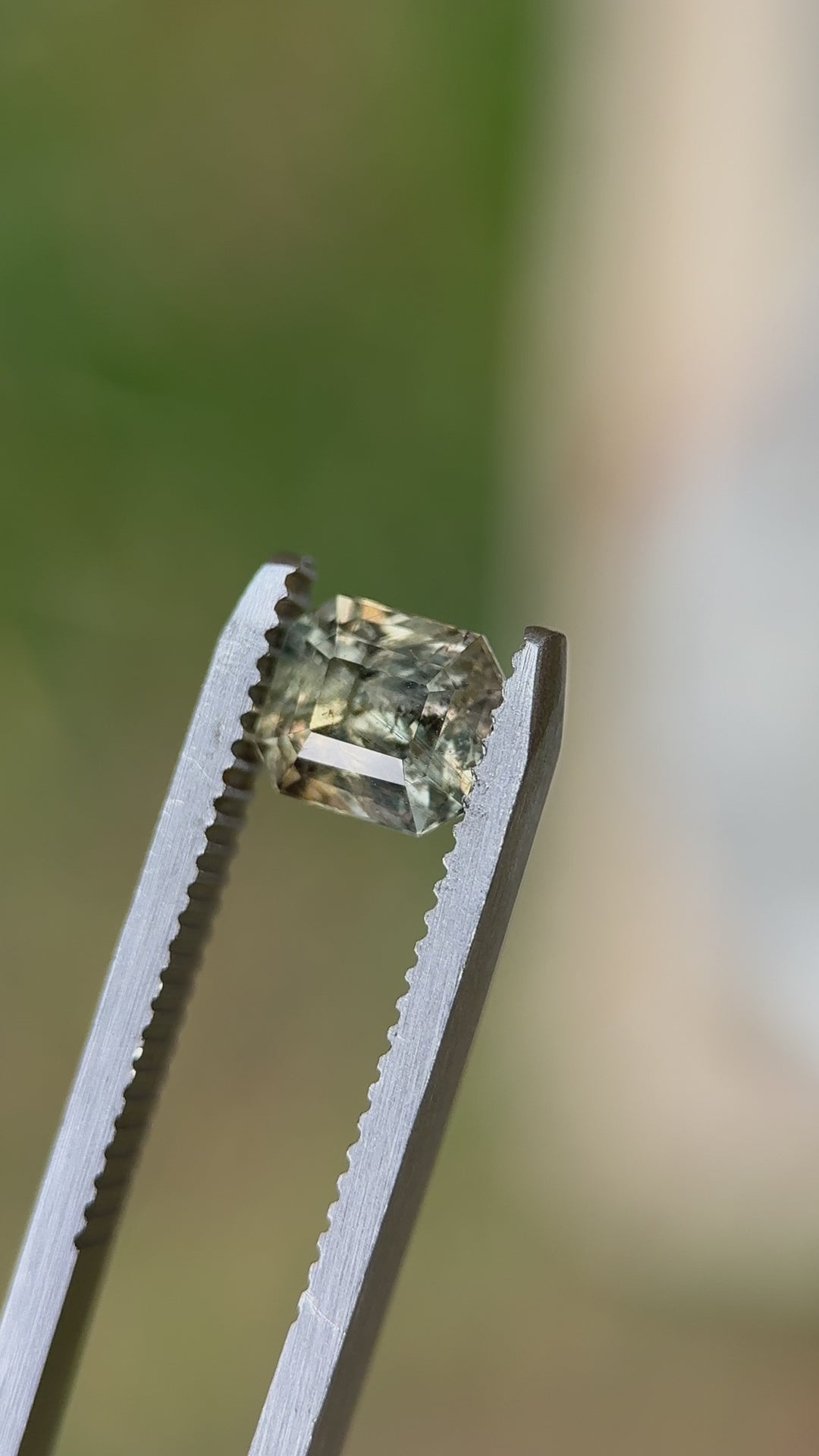 Macro daylight video of 1.67CT sapphire in tweezers, revealing shifting colors from earthy green to red as lighting changes, precision squared emerald cut, unheated and ethically sourced from Umba River, Tanzania
