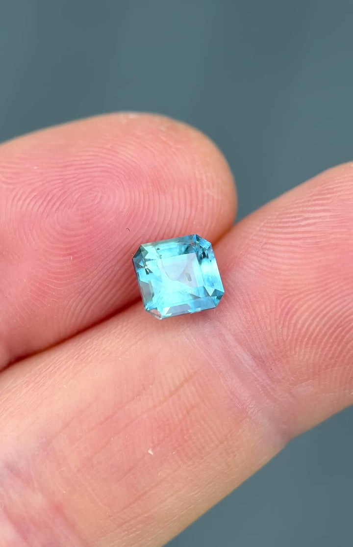 1.75ct Asscher cut Montana sapphire rotating in hand, revealing shifting greenish teal and sky blue tones.