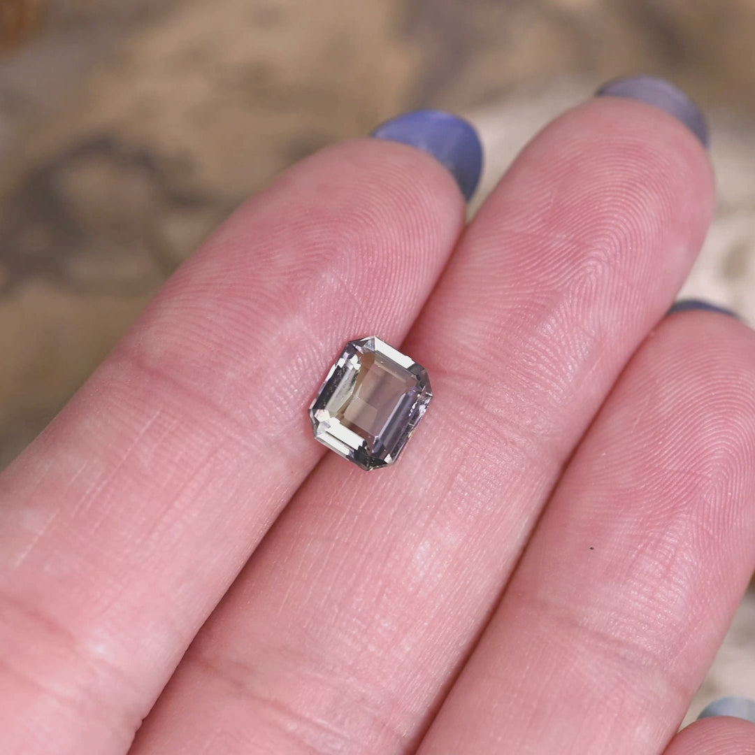 1.67 carat teal blue green purple Tanzanite modified emerald cut rotating on hand under natural light, precision faceted Merelani Hills gemstone showing vivid color zoning and step cut brilliance for custom jewelry