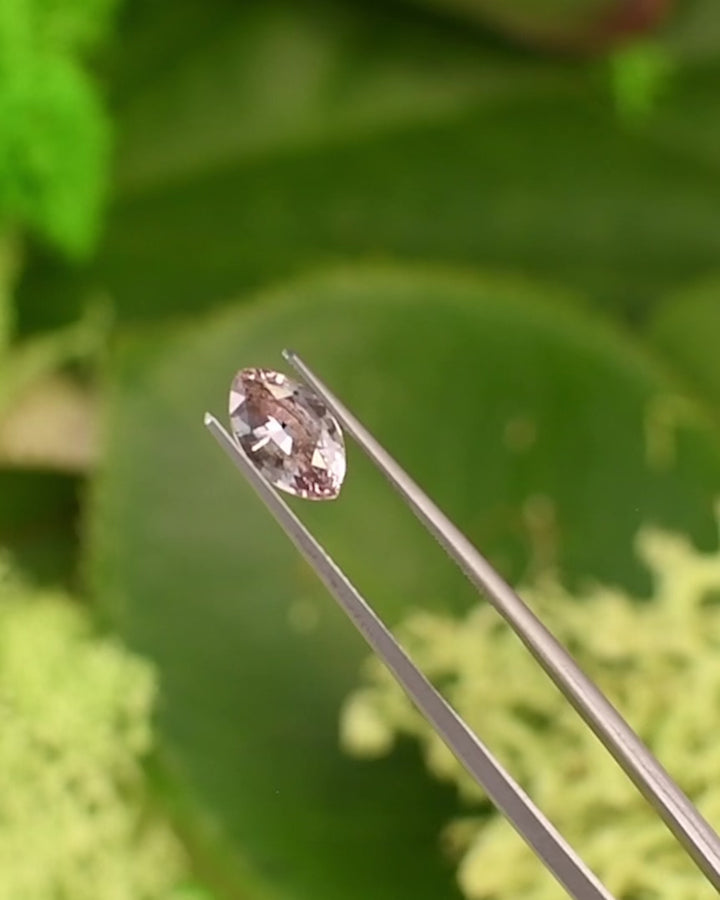 Macro video of 1.32CT salmon pink and peach sapphire rotating in gemstone tweezers under natural light, revealing luster, clarity, and color depth of the precision marquise mixed cut, unheated sapphire from Sakaraha, Madagascar.