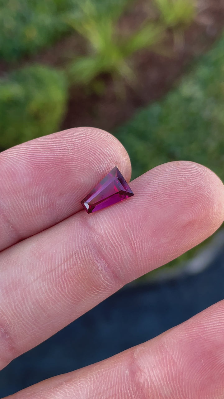 Video showcasing a 2.02-carat garnet gemstone with tapered baguette cut, rotating to reveal its natural red and purple brilliance.
