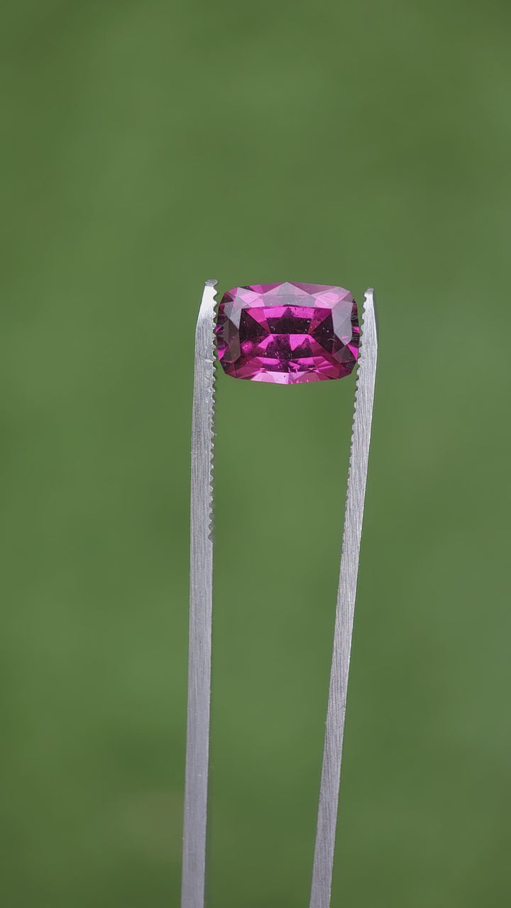 Video demonstration of a 4.29-carat garnet with a geometric modified cushion cut, capturing its vivid purple, pink, and red colors under various lighting conditions. The garnet, originating from Mombo, Tanzania, is displayed in its natural, untreated state, highlighting its unique clarity and color richness.