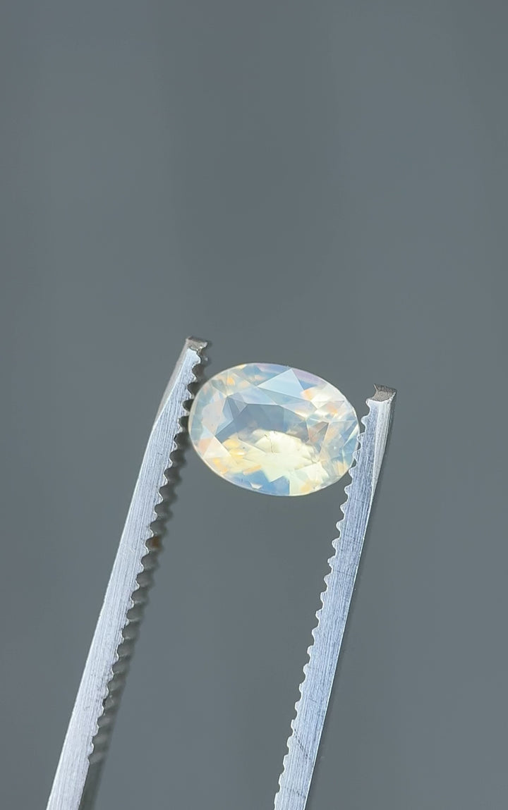 Rotating video of a 1.50 carat untreated Madagascar sapphire in tweezers, capturing the shimmer of its peach, opalescent, and faint blue colors in natural light