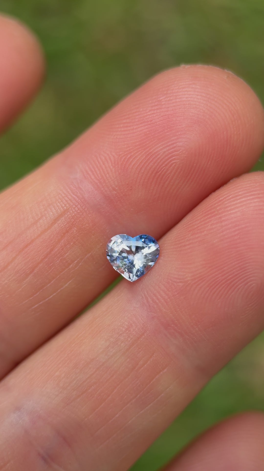 1.30-carat Madagascar parti sapphire resting on fingers, heart cut glimmering with blue and icy white hues under natural light – heated treatment.