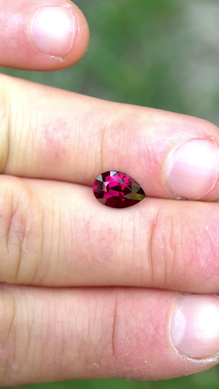 Handheld video of garnet between fingers outdoors, emphasizing size, depth of color, and the poval cut's lively sparkle