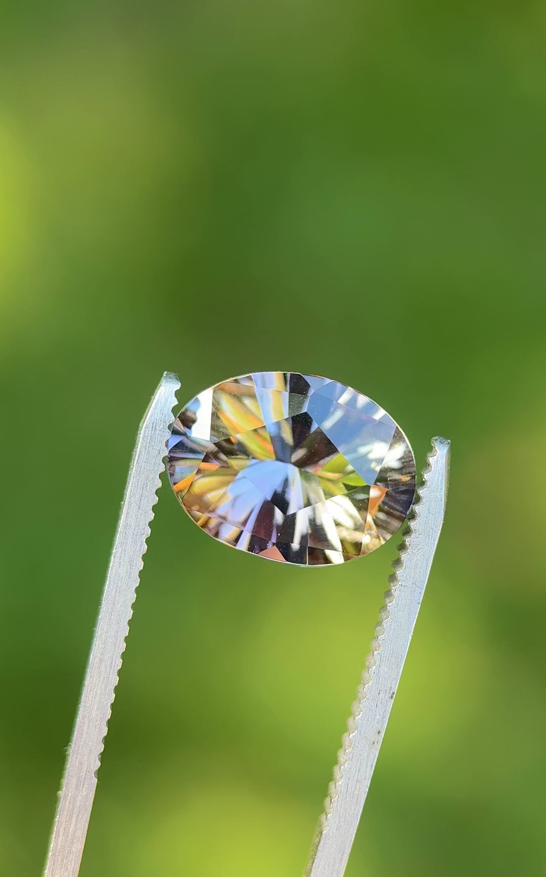 360-degree rotating video of a 4.78ct fancy Tanzanite in tweezers, capturing its dynamic color shift from peach to teal, purple, and yellow in an oval concave cut