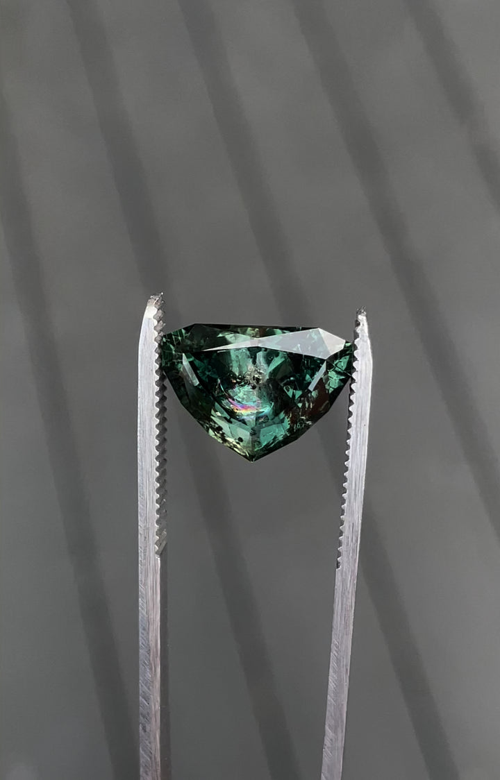 A detailed view of a 7.06-carat sapphire with a bluish-green to gray-purple color change, featuring a modified shield brilliant cut, ethically sourced from Montana.
