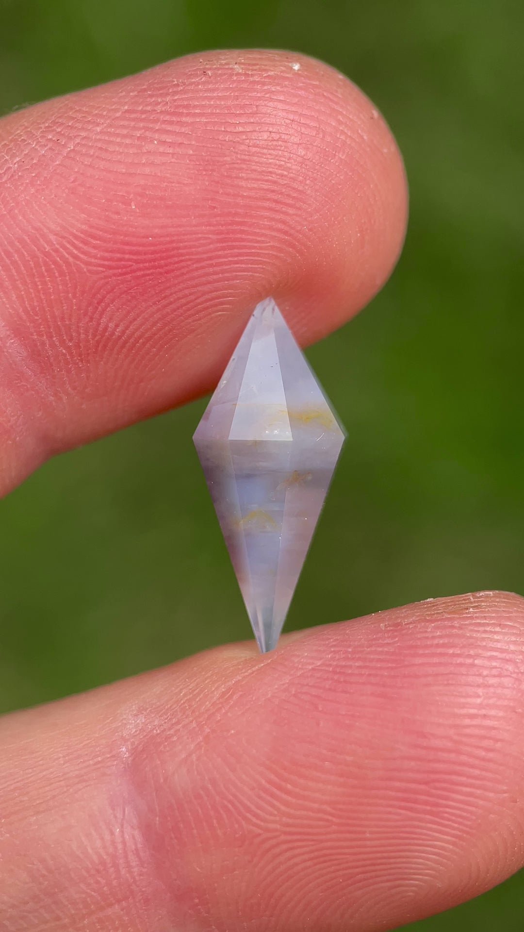 Video of 8.00 ct earthy periwinkle sapphire rotating between fingers, capturing light reflection and intricate rhombohedral faceting.
