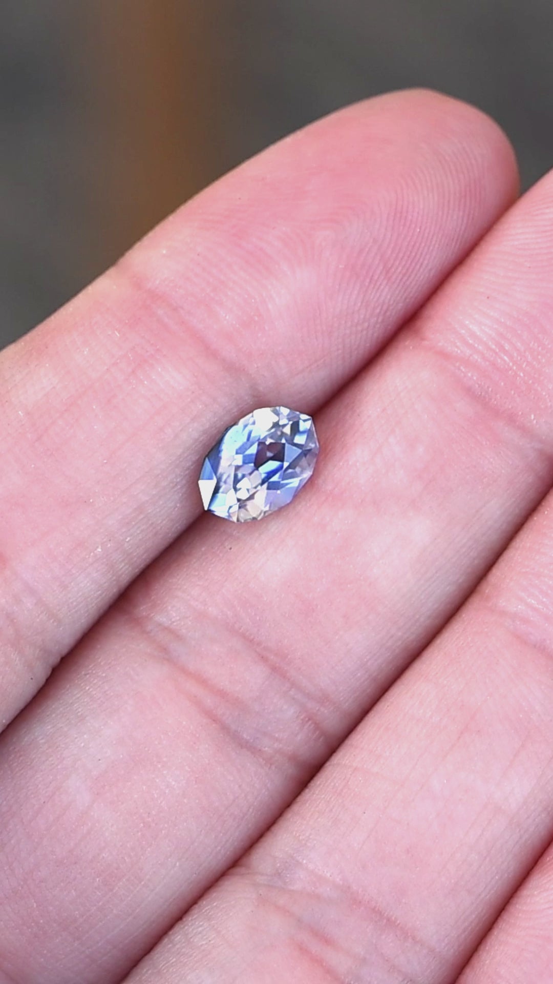 1.85ct blue and white parti sapphire in a custom moval brilliant cut from Sri Lanka rotating on fingertips under natural light.