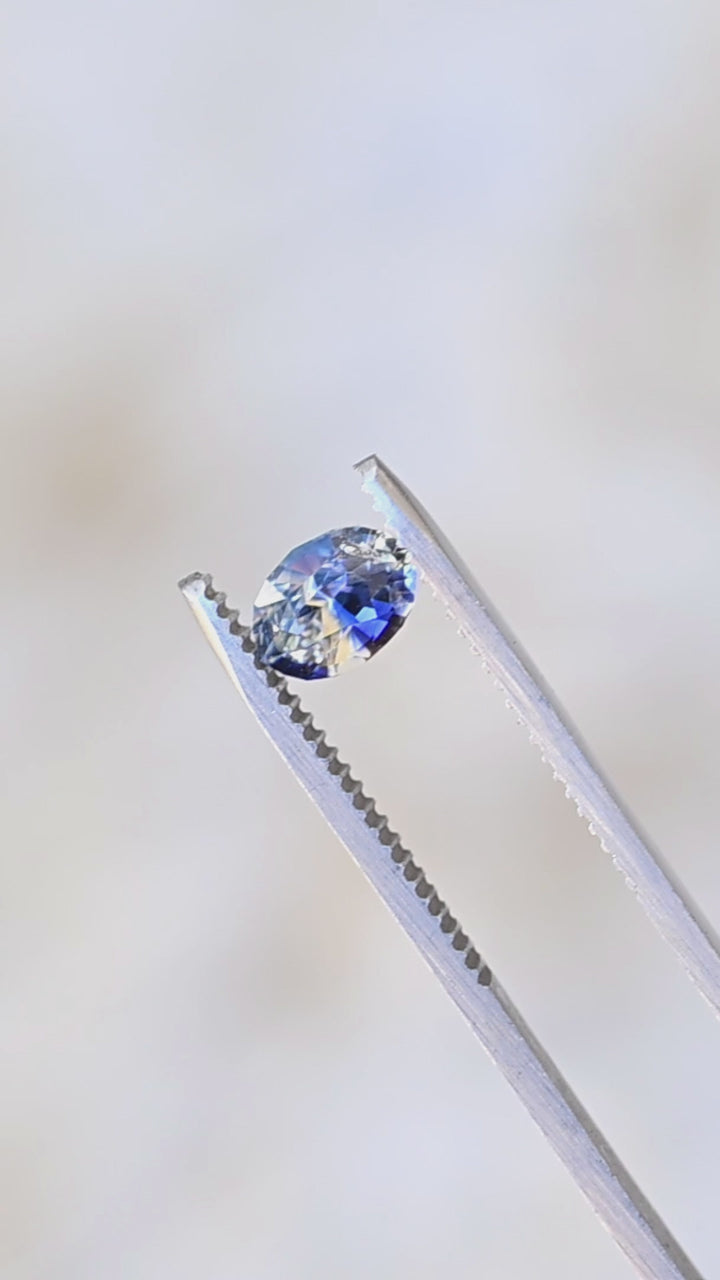 1.60ct blue and white bi color parti sapphire from Sri Lanka rotating in gem tweezers under natural light.