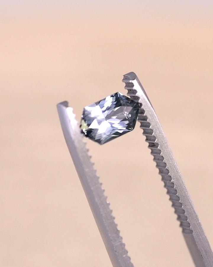 Video of a 1.11 carat seafoam grey blue sapphire rotating in gem tweezers, elongated hexagon mixed cut revealing light return, facet geometry, and natural unheated color from Sakaraha Madagascar