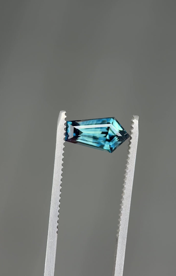 360-degree video of a 2.11-carat banded teal blue parti sapphire in a precision elongated shield step cut from Madagascar, rotating to show brilliance, step facets, and color zoning.