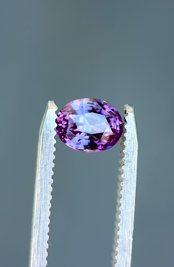 Natural Sri Lankan sapphire turning in tweezers, showcasing vivid pink-purple color and exceptional light return.