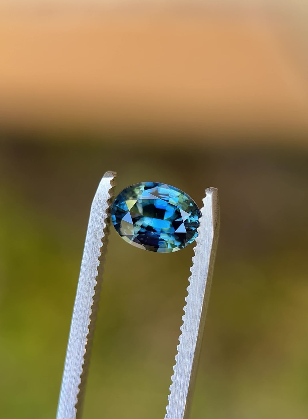 Video of 1.55CT yellow teal blue parti sapphire rotating in gemstone tweezers, showing color shifts between yellow, teal, and blue as light dances across the oval mixed cut, unheated sapphire from Sakaraha, Madagascar.