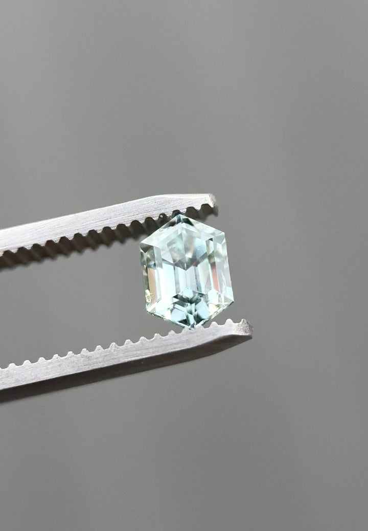 Video of a 1.22 carat Montana sapphire slowly rotated in jeweler’s tweezers, revealing precision elongated hexagon step cut facets and a natural color shift from light seafoam green to grey silver under changing light.