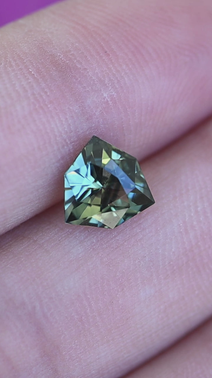 Rotating 2.03 carat bluish teal green parti sapphire on hand showing color movement, brilliance, and geometric shield cut.