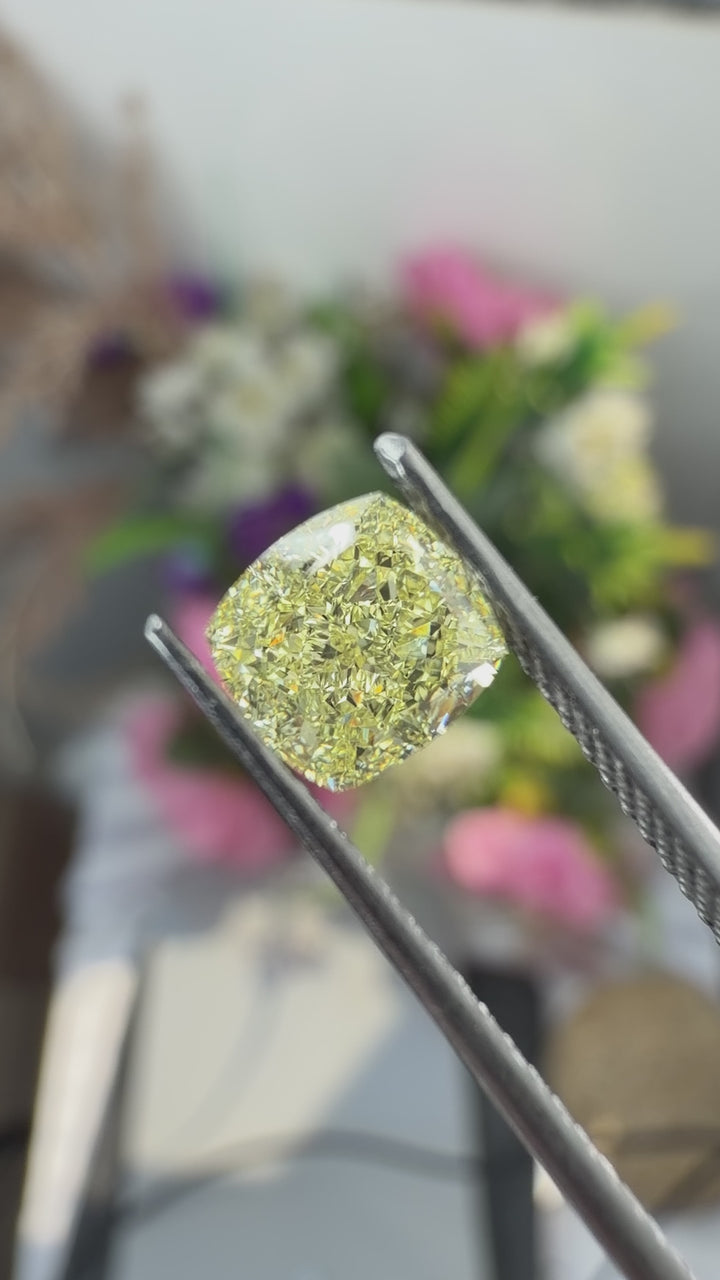 Fancy yellow cushion cut natural diamond held in gem tweezers under natural light