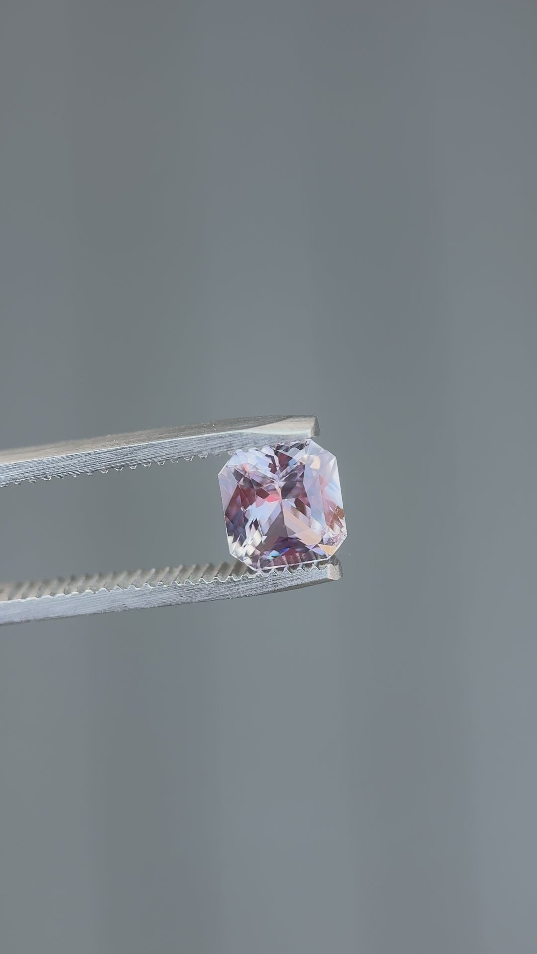 Rotating video of a 2.14-carat lavender sapphire from Madagascar held in gemstone tweezers, showing vibrant light reflection through the radiant octagonal cut with a blurred natural background.
