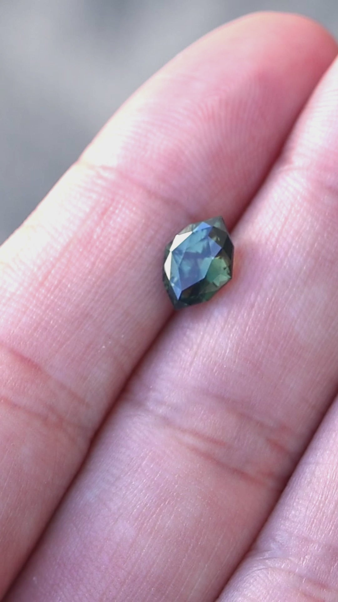 1.68ct green teal geometric marquise sapphire from Diego, Madagascar rotating on finger tips under natural light.