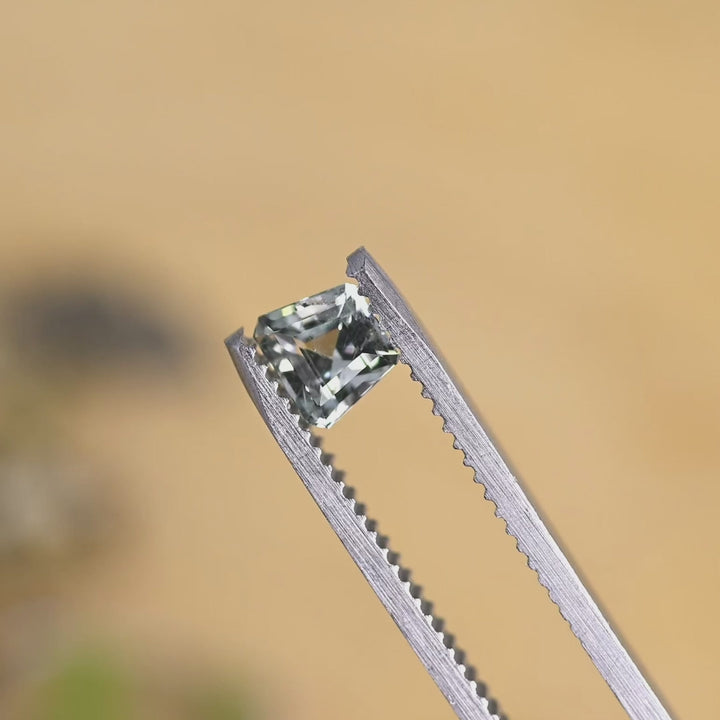 Heated El Dorado Bar seafoam sapphire turned in tweezers under natural light, emphasizing its architectural trapezoid shape and reflective step pattern.