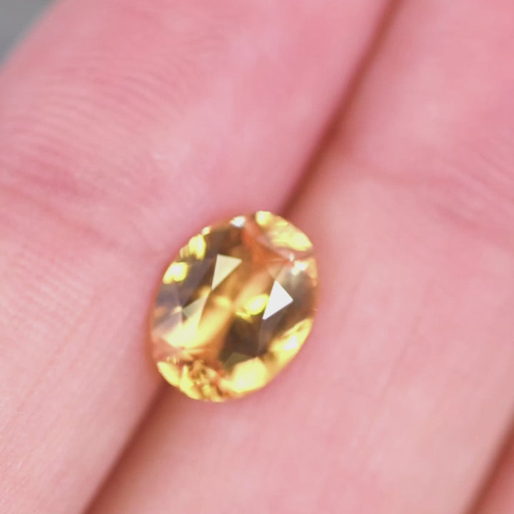 Handheld video of an orange red oval sapphire turning under light to reveal brilliance, facet pattern, and warm sunset hues from Ratnapura, Sri Lanka