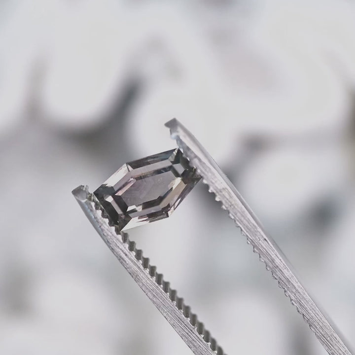 Close-up video of 1.15 carat purple pink gray Montana sapphire in tweezers, hexagon portrait cut showing sparkle, color zoning, and natural inclusions, untreated USA origin.
