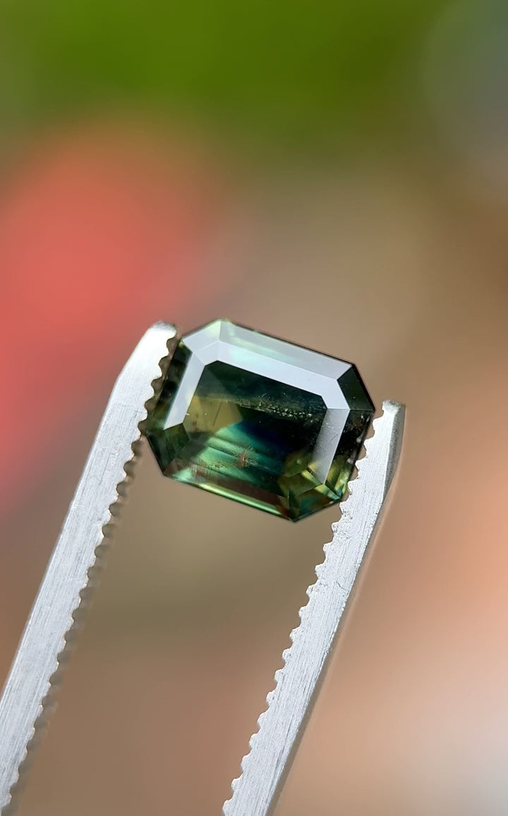 Video of 2.14 carat parti sapphire rotating in tweezers, revealing peacock, teal, yellow, and blue flashes.