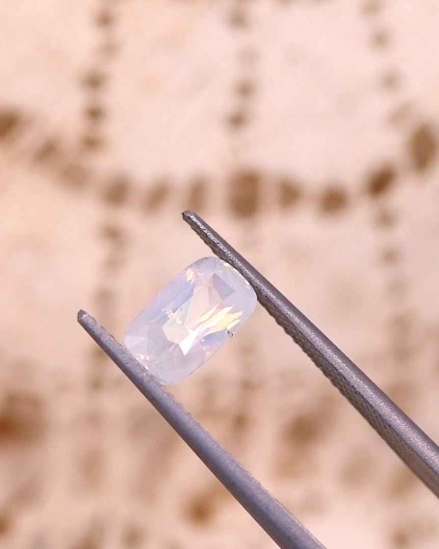 Video of 2.05CT opalescent peach sapphire rotating in gemstone tweezers, revealing its soft luster, light refraction, and cushion cut brilliance of the untreated sapphire from Sakaraha, Madagascar.