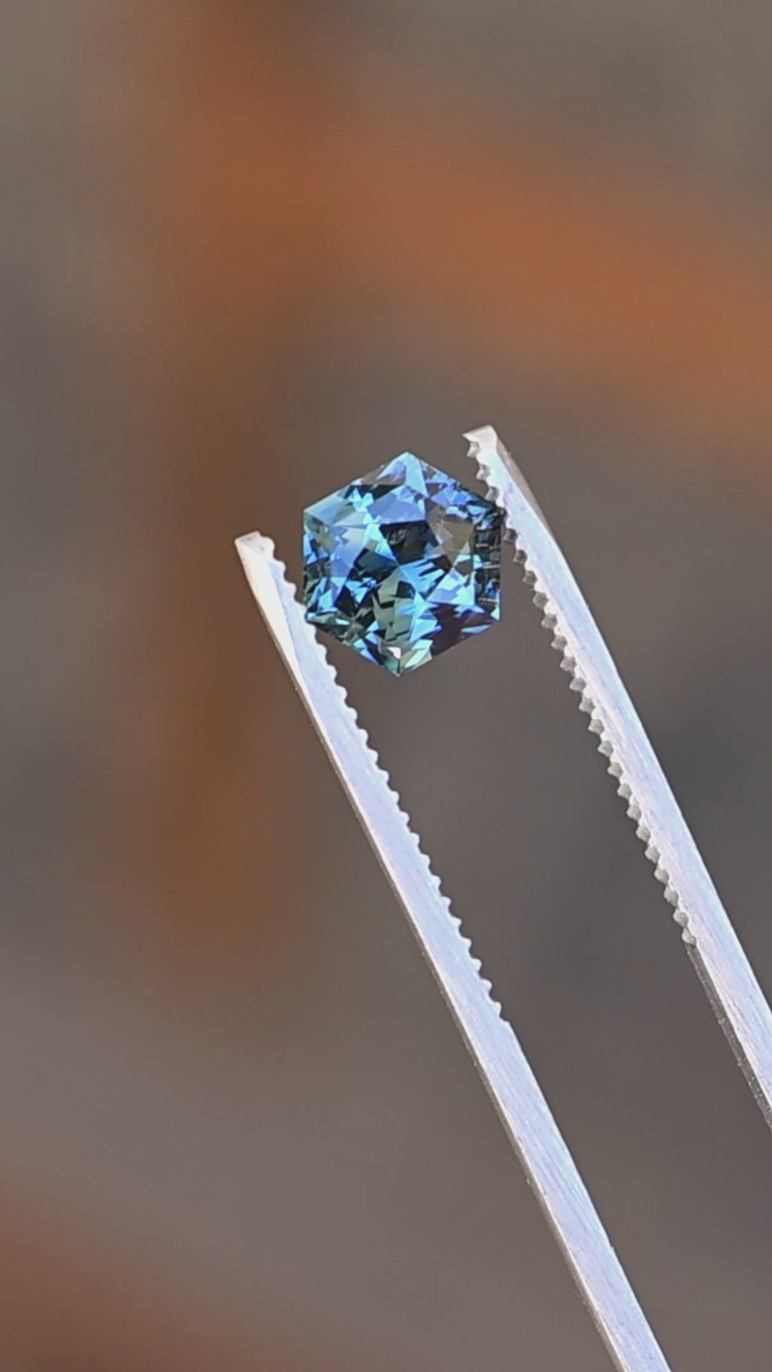2.03ct blue teal precision hexagonal cut sapphire rotating in gem tweezers under natural light.