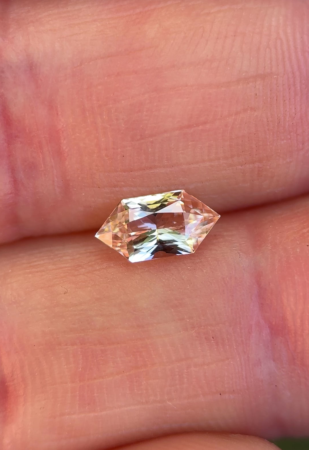 Hand-held salmon pink peach sapphire showing scale, soft color shifts, and brilliance in natural light.