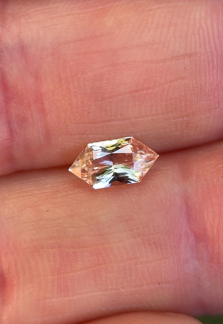Hand-held salmon pink peach sapphire showing scale, soft color shifts, and brilliance in natural light.