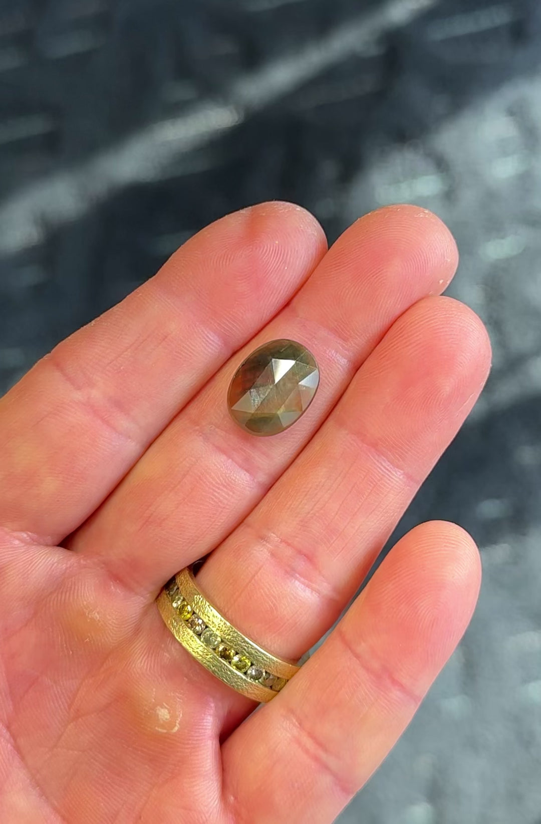 Large oval orange and green parti sapphire rotated in hand, showing shifting moss green to amber tones across the domed rose-cut surface.