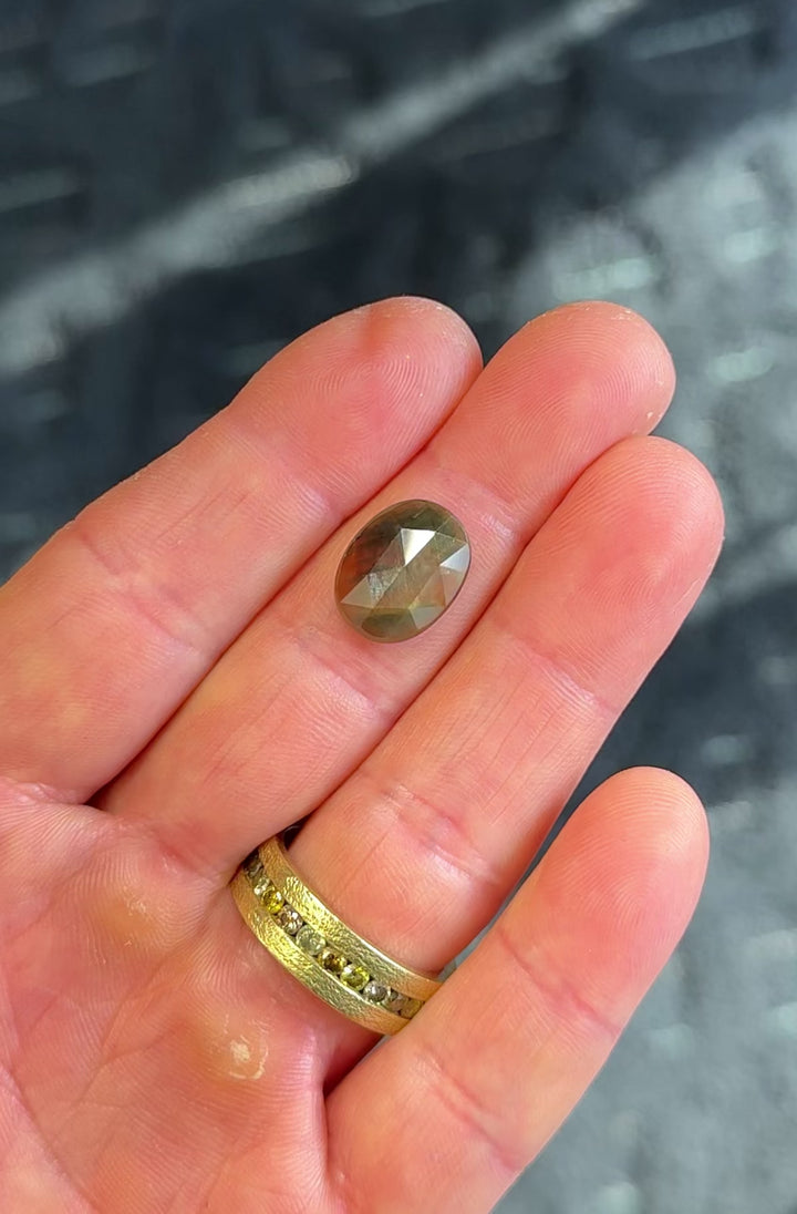 Large oval orange and green parti sapphire rotated in hand, showing shifting moss green to amber tones across the domed rose-cut surface.