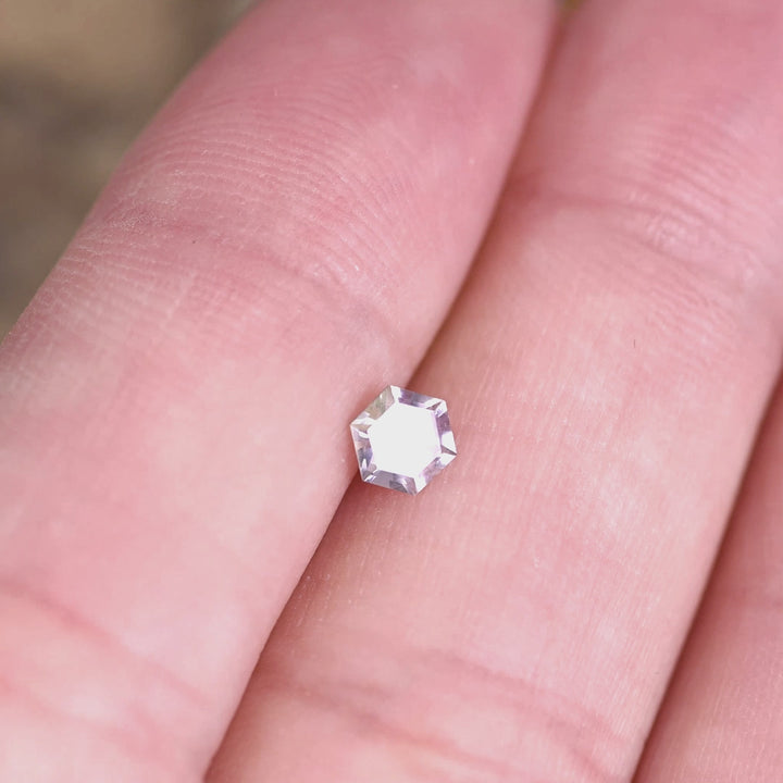 0.42 carat purple pink Montana sapphire hexagon step cut rotating on hand under natural light, untreated El Dorado Bar gemstone showing pastel color shift and crisp geometric reflections for custom jewelry