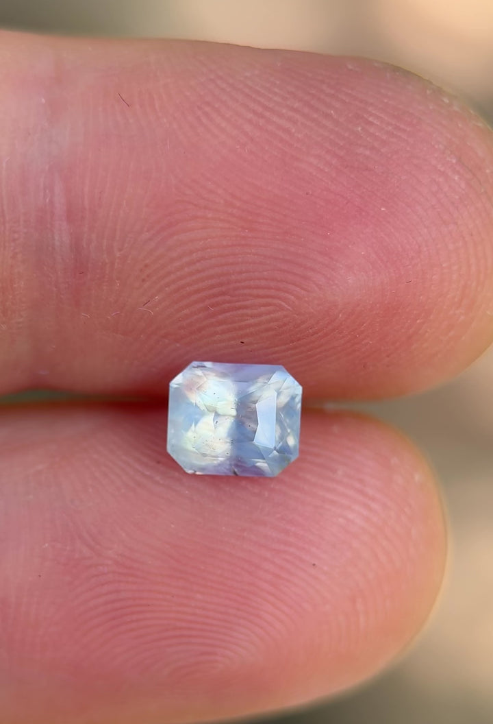 Rotating 1.58CT Madagascar sapphire resting on fingers, showing soft silver blue hues and radiant clarity