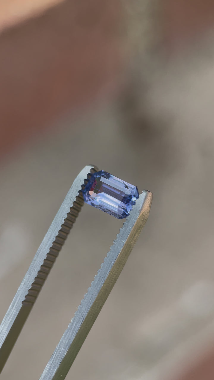 A video showcasing a 1.26-carat sapphire with violet-blue hues, cut in a Modified Emerald style, displayed under natural light to emphasize its brilliance.