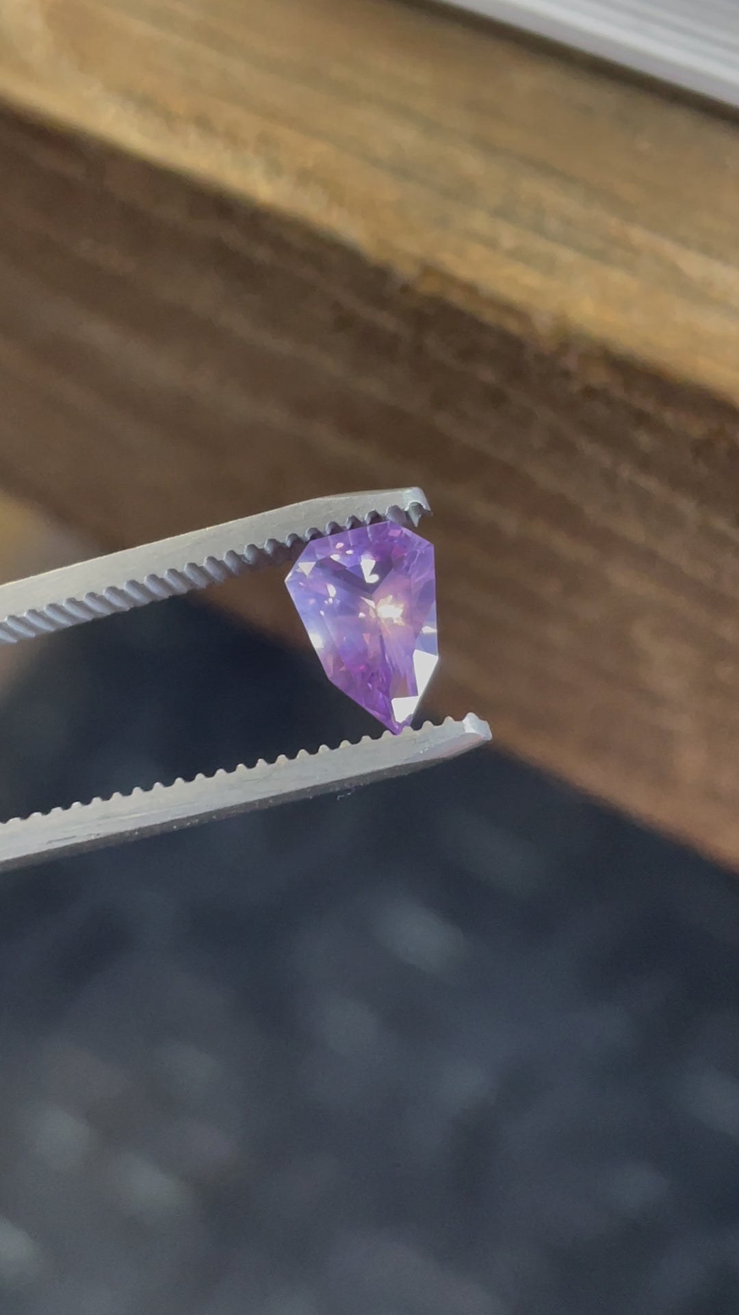 A rotating view of a pink and purple opalescent sapphire in a custom geometric shield cut, highlighting its facets and color transitions under natural light.