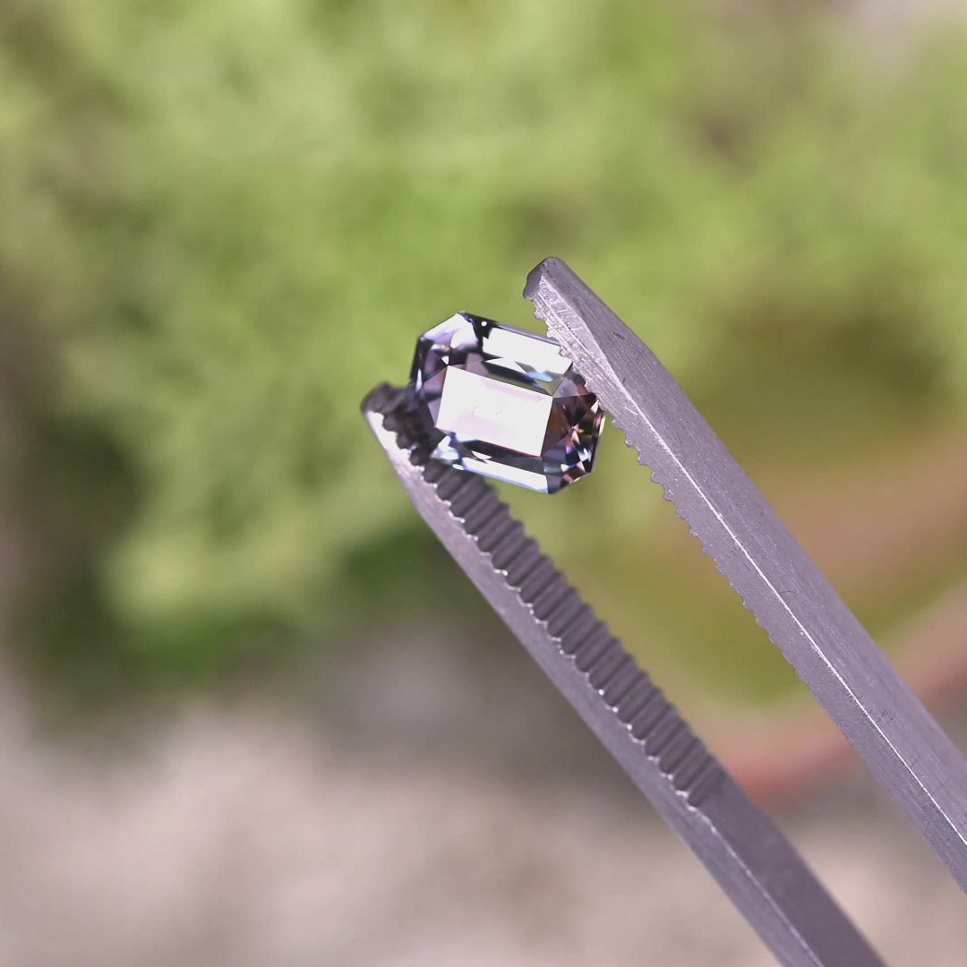 Close-up video of 1.56ct purple teal champagne Tanzanite modified radiant held in tweezers, custom precision cut gemstone from Tanzania displaying sharp bevels, high clarity and vivid trichroic brilliance