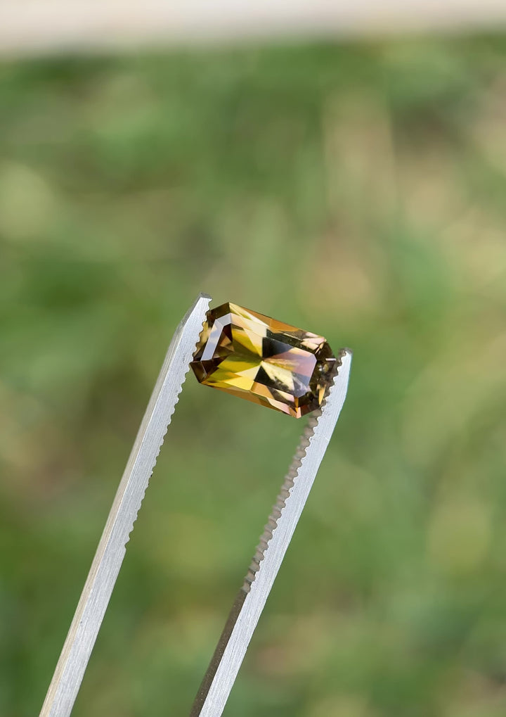 Macro close-up video of 2.63CT fancy Tanzanite turning in tweezers, showing the interplay of purple, pink, and golden hues across radiant cut facets, ethically sourced and untreated from the Merelani Hills, Arusha Region, Tanzania.