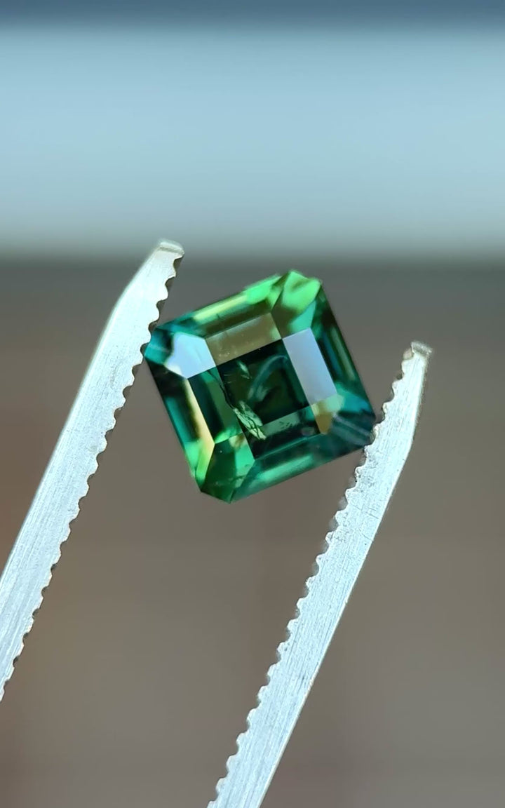 Natural Kenyan sapphire turning in tweezers, showcasing precision step faceting, deep teal saturation, and geometric symmetry.