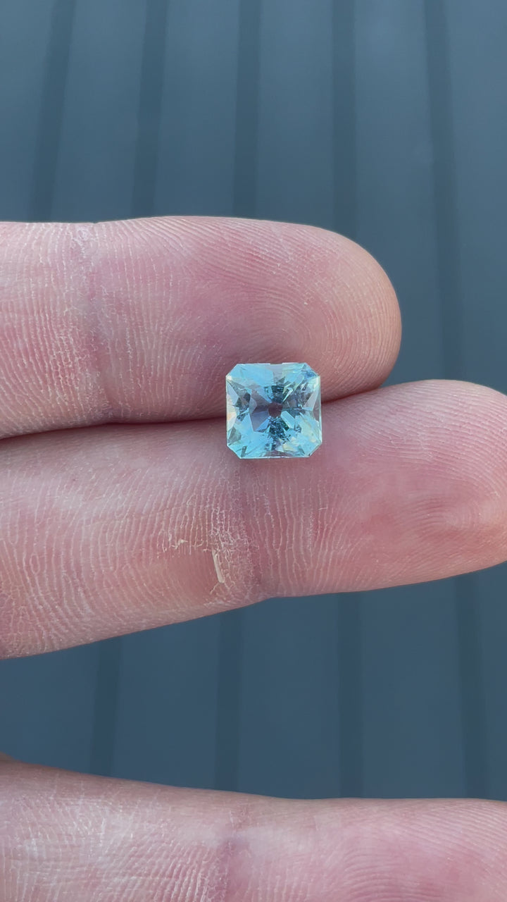 A rotating view of a blue aquamarine gemstone with seafoam undertones, weighing 2.87 carats, capturing its brilliance and antique cushion cut in natural light.