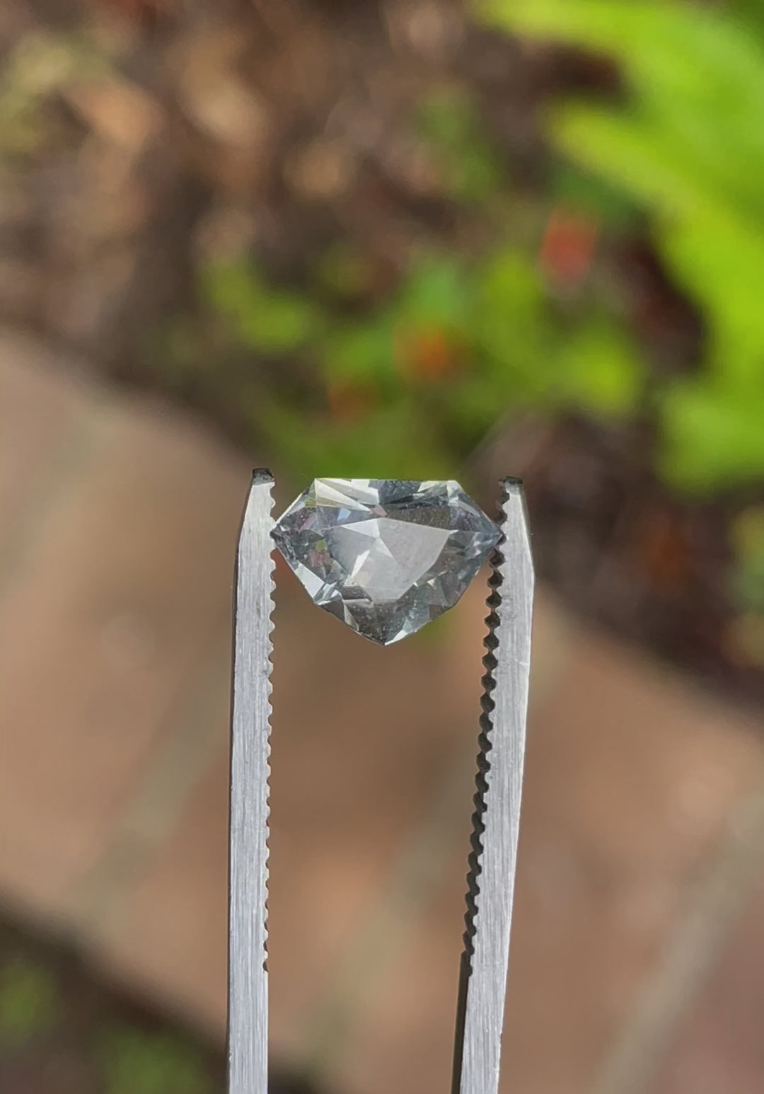 A rotating view of a 2.11-carat sapphire with a custom shield cut, displaying its striking mix of gray, yellow, and teal colors under natural lighting. The video highlights the stone's intricate faceting and untreated clarity.