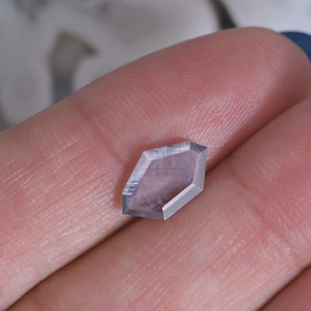 Rotating video of a 1.22ct purple brown gray parti sapphire in a geometric shield portrait cut, revealing natural color zoning and untreated clarity from Sri Lanka.