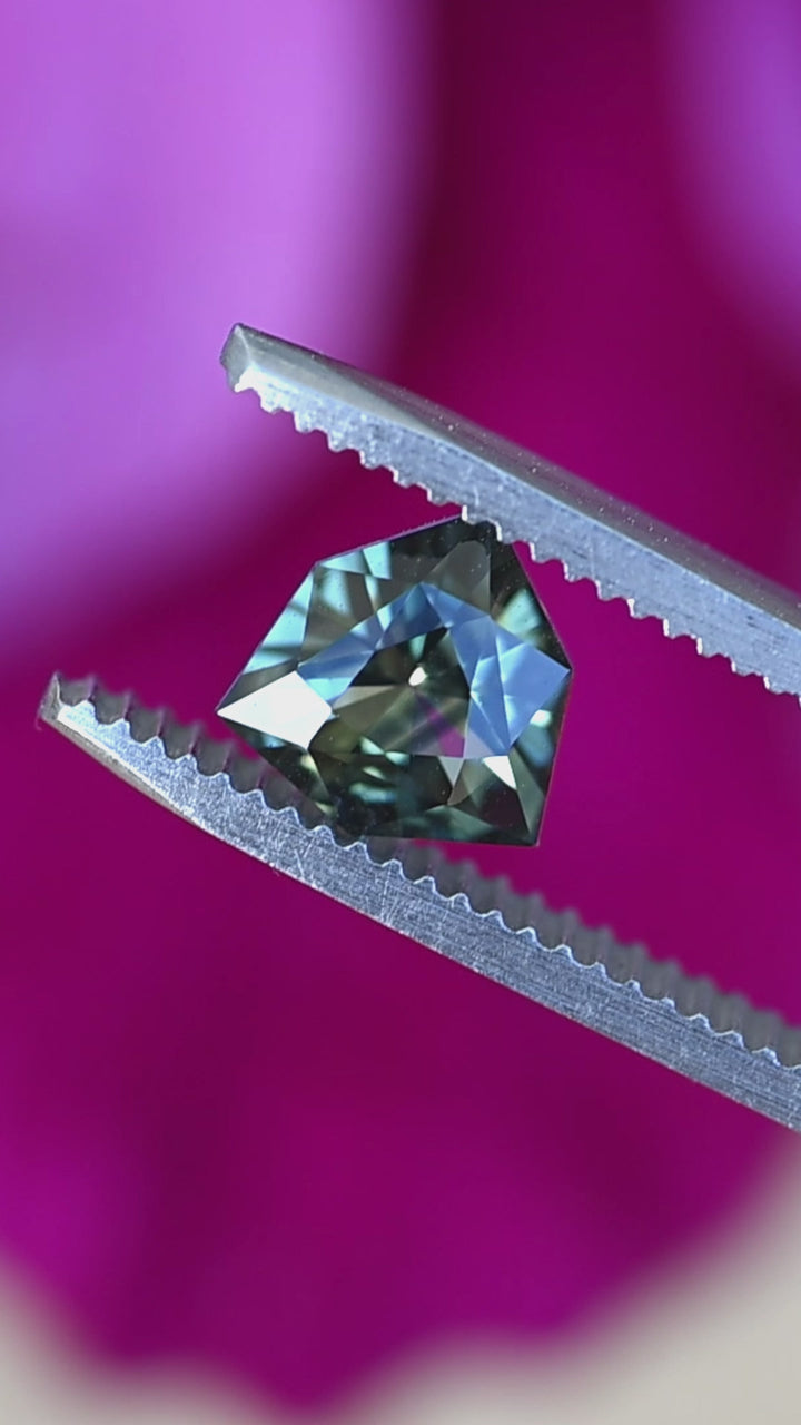 Bluish teal green parti sapphire rotating in tweezers showing precision faceting, heated treatment, and shifting blue-green color.