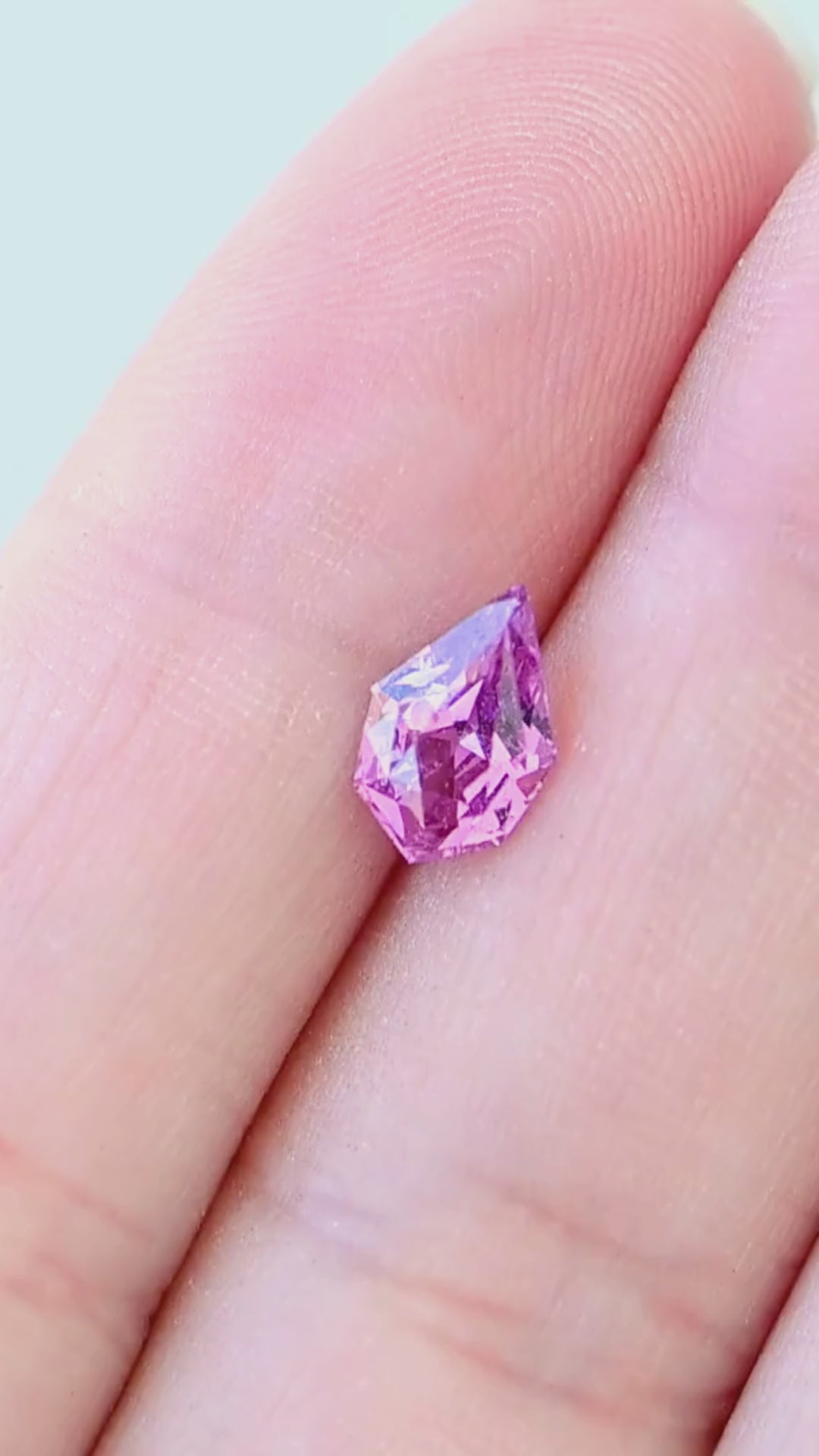 1.27 carat untreated pink-purple sapphire shown moving on a hand, revealing vivid fuchsia, orchid and violet flashes throughout its precision geometric pear cut.