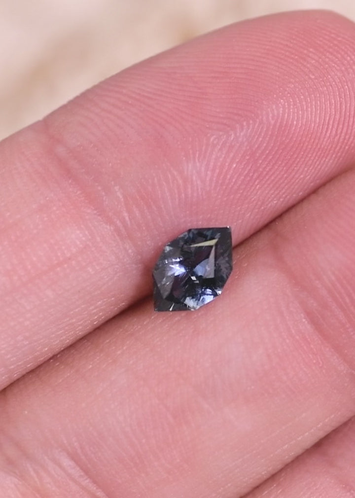 Loose denim blue sapphire turning in tweezers, revealing light reflection and facet pattern in a modified brilliant marquise cut from Madagascar.