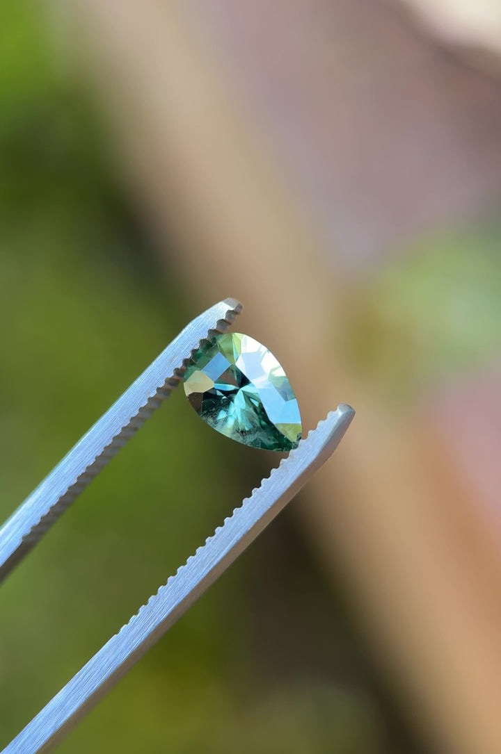 Video of a lagoon teal green Montana sapphire rotating in tweezers, revealing the shield step cut geometry, facet reflections, and heated sapphire brilliance.