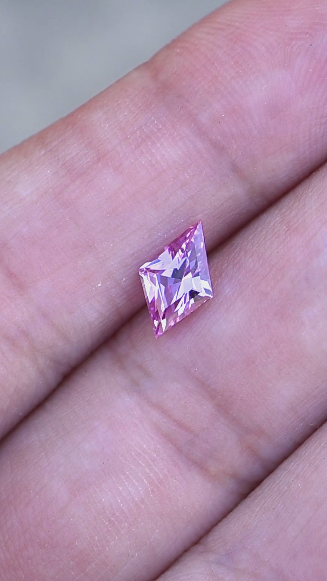 1.15ct hot pink custom kite rhombus cut sapphire rotating on finger tips under natural light.