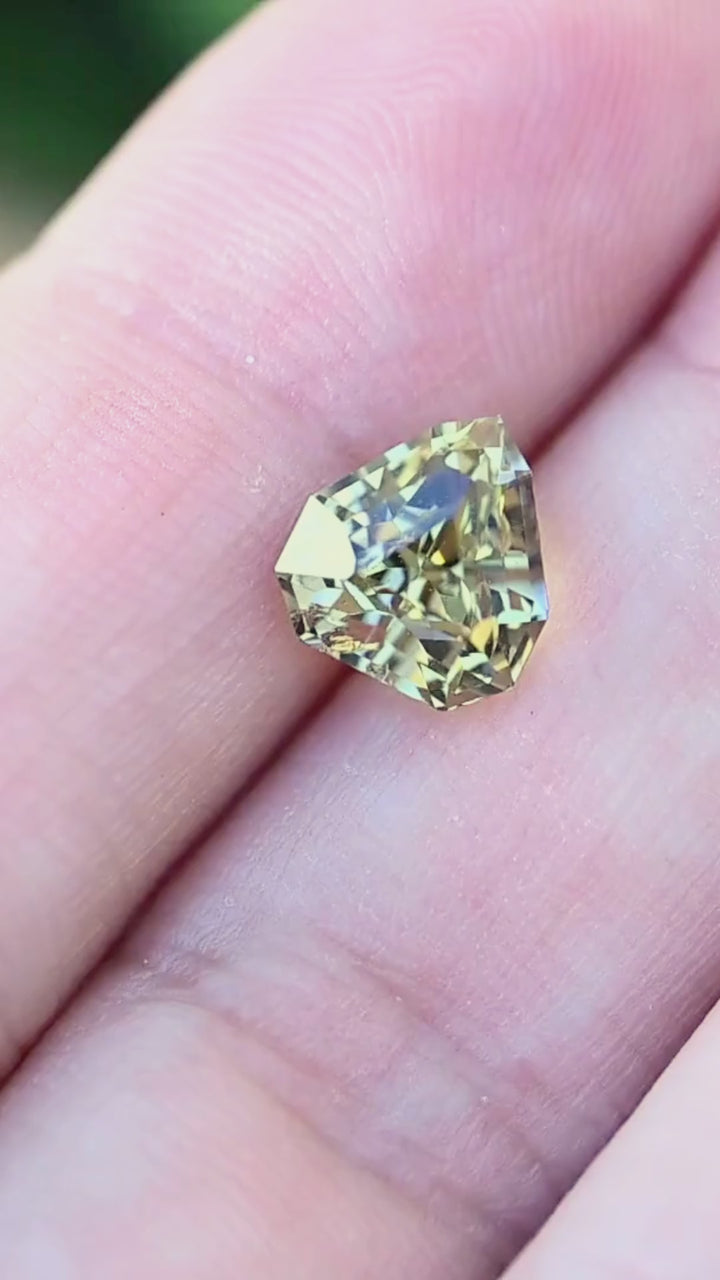 A 2.42 carat untreated Tanzanite rotating on fingertips in natural light, revealing vivid pleochroic shifts between teal, green, and golden yellow with exceptional brilliance.