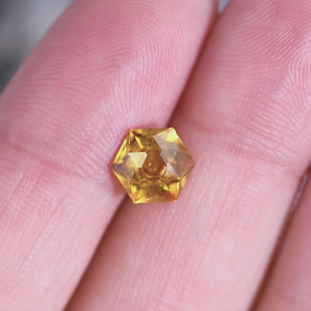Close-up video of 1.88 carat heated Montana sapphire hexagonal brilliant cut displaying fiery orange yellow flashes and geometric sparkle pattern